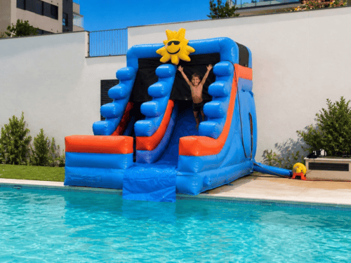 Tobogán acuático hinchable azul y naranja con sol sonriente, junto a piscina, alquiler en Valencia